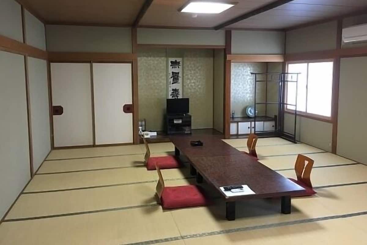 A traditional tatami room with a low table and chairs, a sliding door, and a television.
