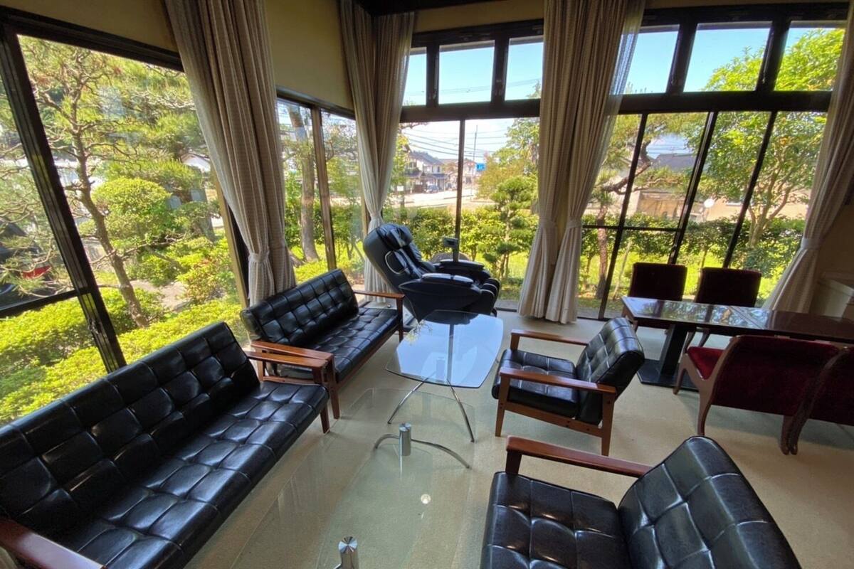 A room with a sofa, chairs, a table, and large windows with curtains.