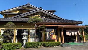 Ein traditionelles japanisches Gebäude mit einem Ziegeldach, einem Steinlaternen und einem Schild, das Besucher in Notojima willkommen heißt.