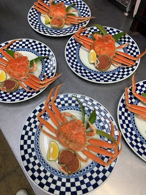 Una mesa con varios platos de cangrejo, cada uno con un estampado de cuadros y adornado con limón y hojas verdes.