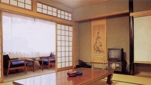 Ein traditioneller japanischer Raum mit Tatami-Matten, einem niedrigen Holztisch, einem Fernseher und einem Shoji-Bildschirm.