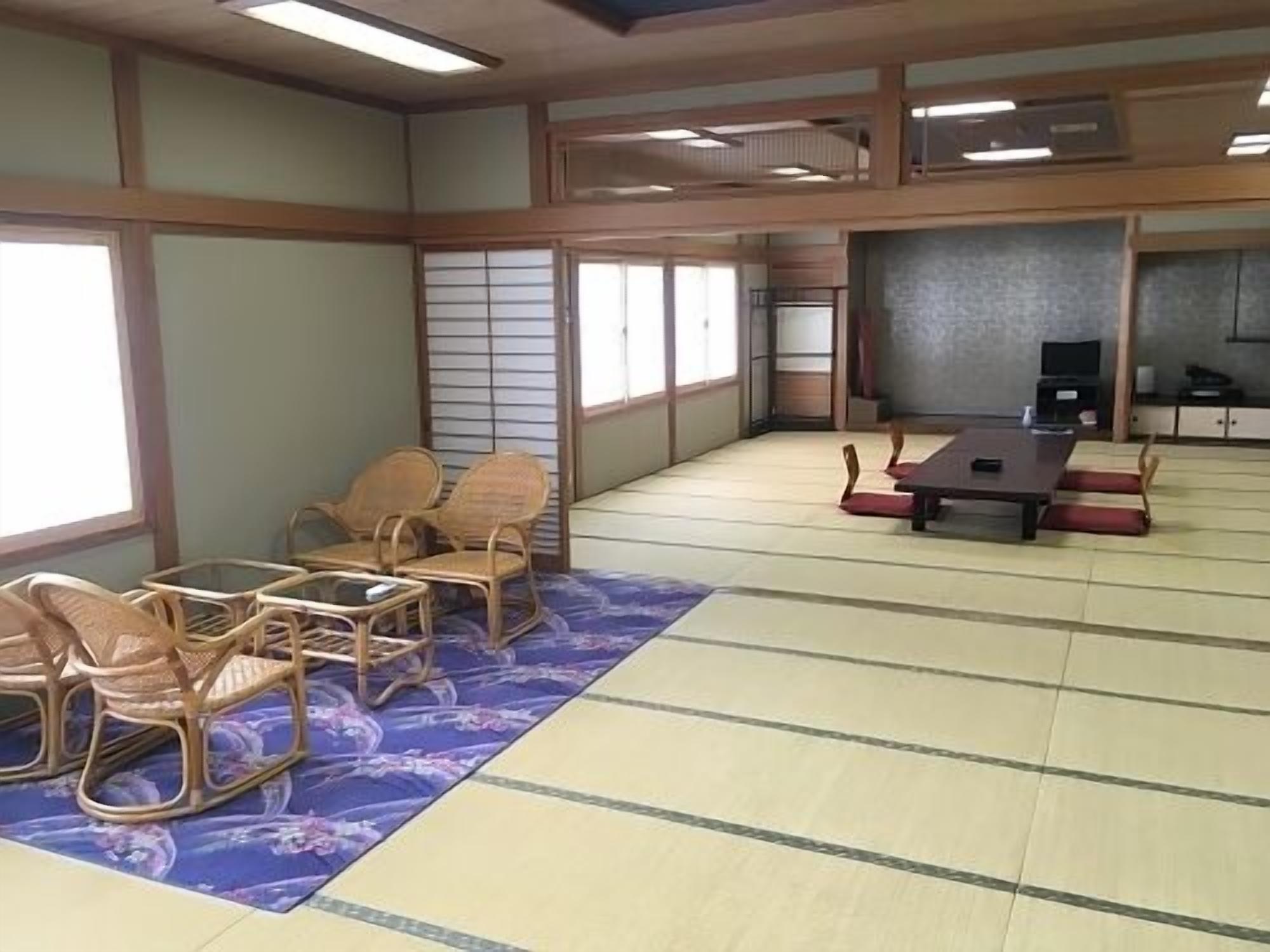 Ein traditioneller Raum mit Tatami-Matten, einem Tatami-Tisch und Stühlen, einem Fernseher und verschiebbaren Türen.