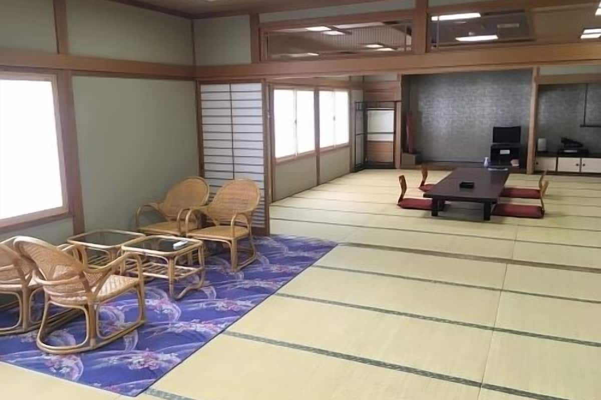 A traditional tatami mat room with a tatami mat table and chairs, a television, and sliding doors.