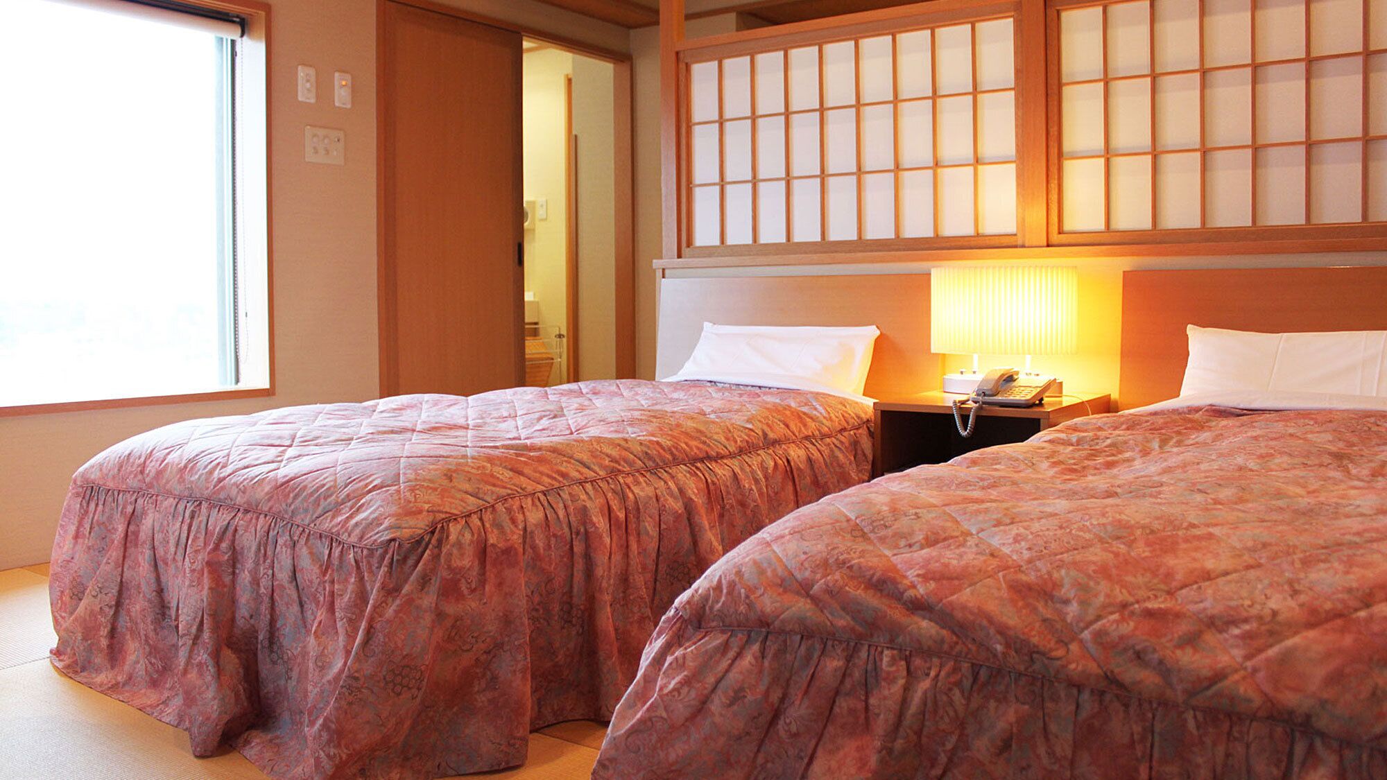 A hotel room with two beds, a nightstand with a phone, and a window with a view.