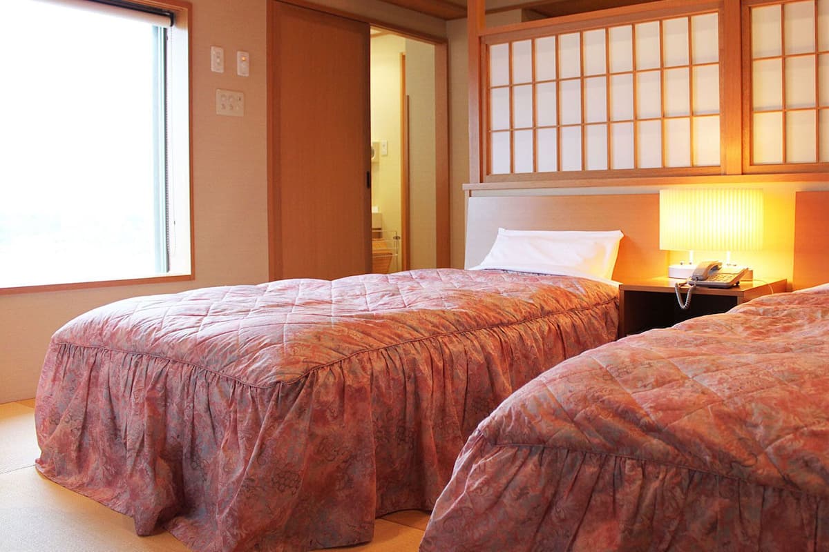 A hotel room with two beds, a nightstand with a phone, and a window with a view.