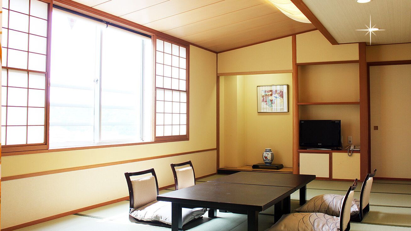 A traditional Japanese room with tatami flooring, a low table, and a television on a cabinet.