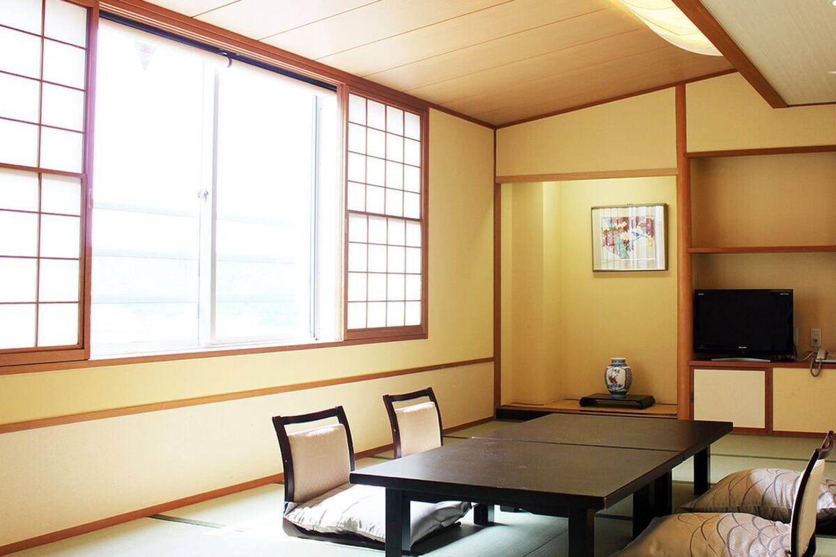 A traditional Japanese room with tatami flooring, a low table, and a television on a cabinet.