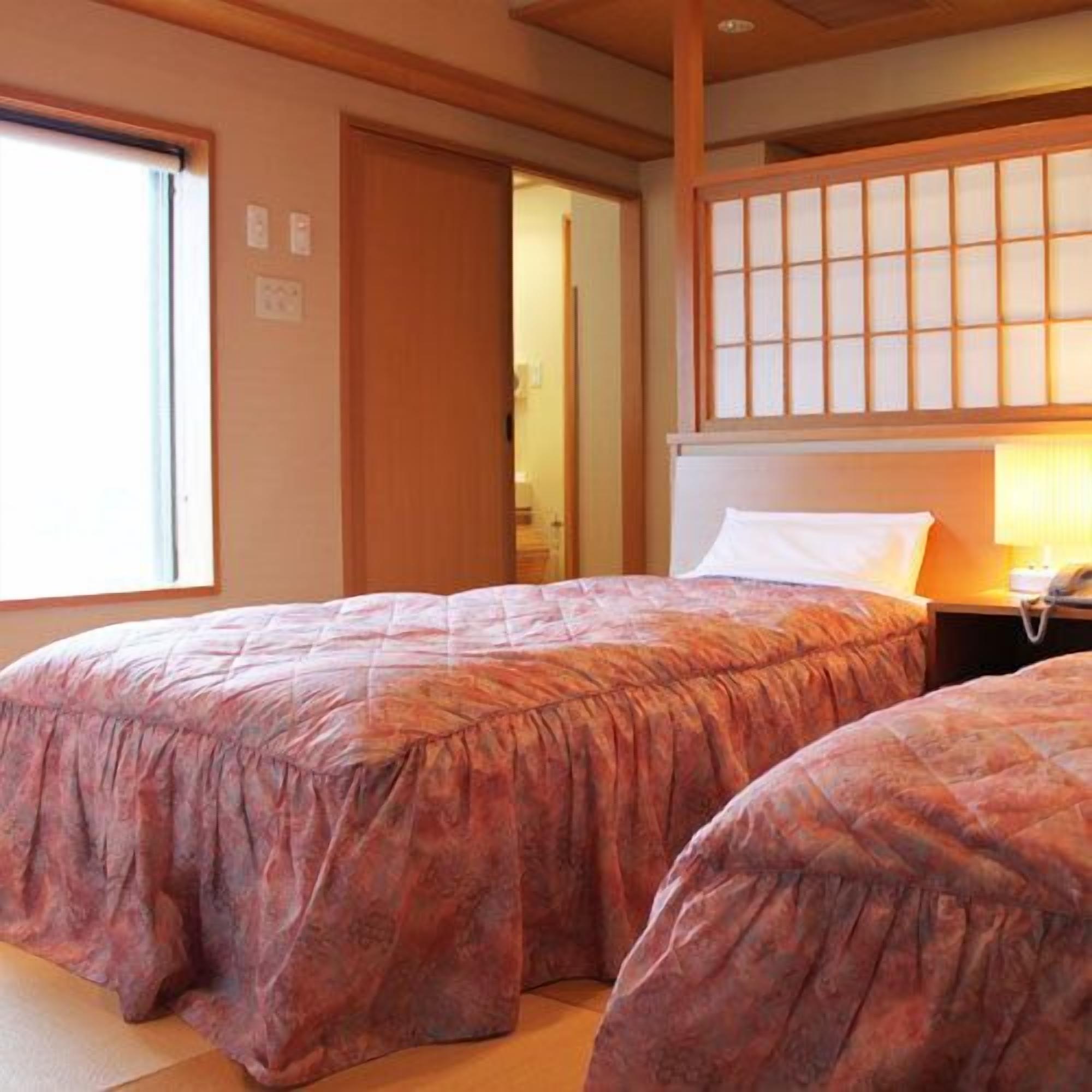 A room with two beds, a wooden ceiling, a window, and a traditional Japanese sliding door.