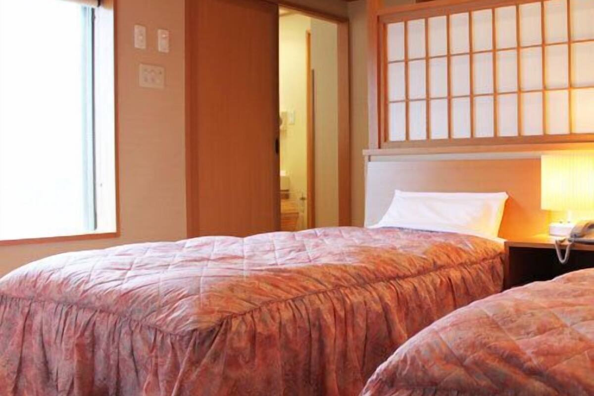 A room with two beds, a wooden ceiling, a window, and a traditional Japanese sliding door.
