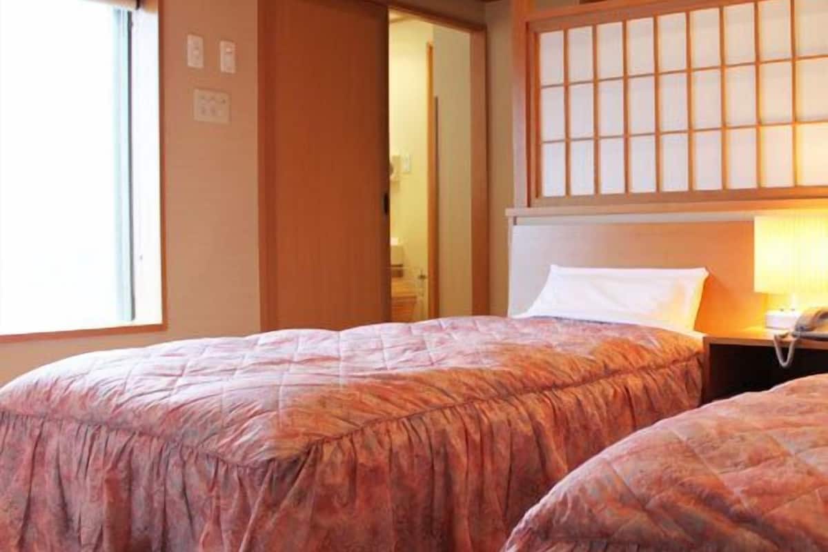 A room with two beds, a wooden ceiling, a window, and a traditional Japanese sliding door.