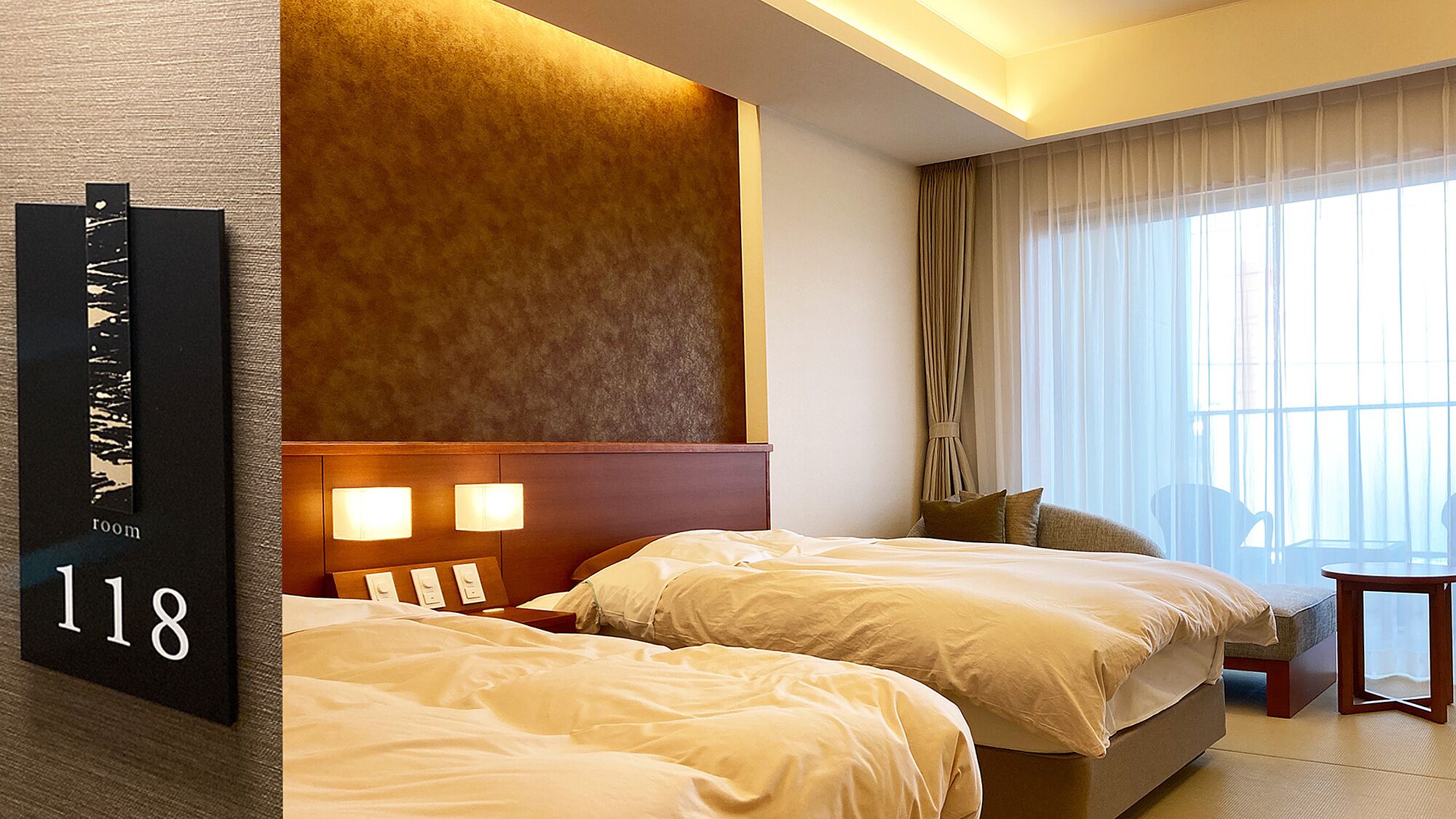 A hotel room with two beds, a large window with curtains, and a wall-mounted sign indicating room number 118.