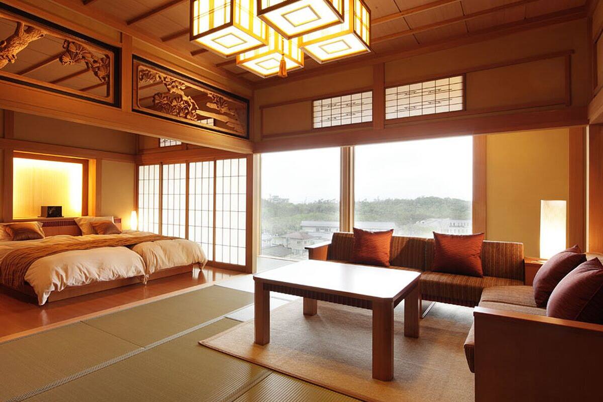 A traditional Japanese-style room with tatami flooring, a low wooden bed, a sofa, and a table.