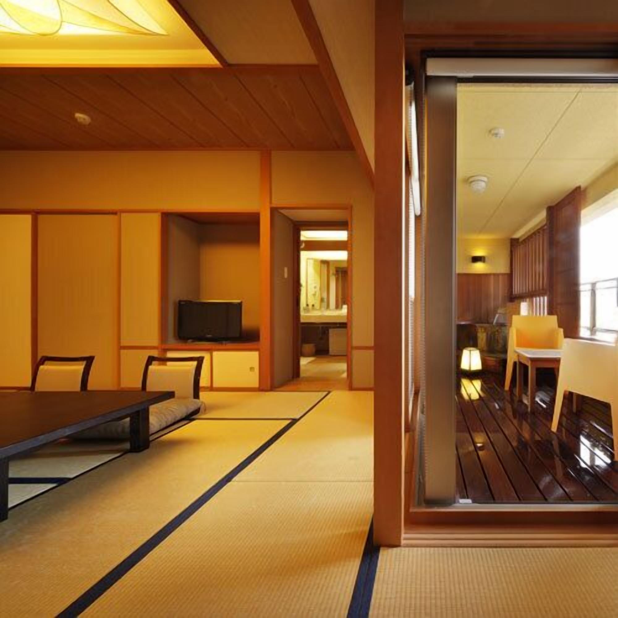 A traditional Japanese-style room with tatami flooring, a low table, chairs, and a television.