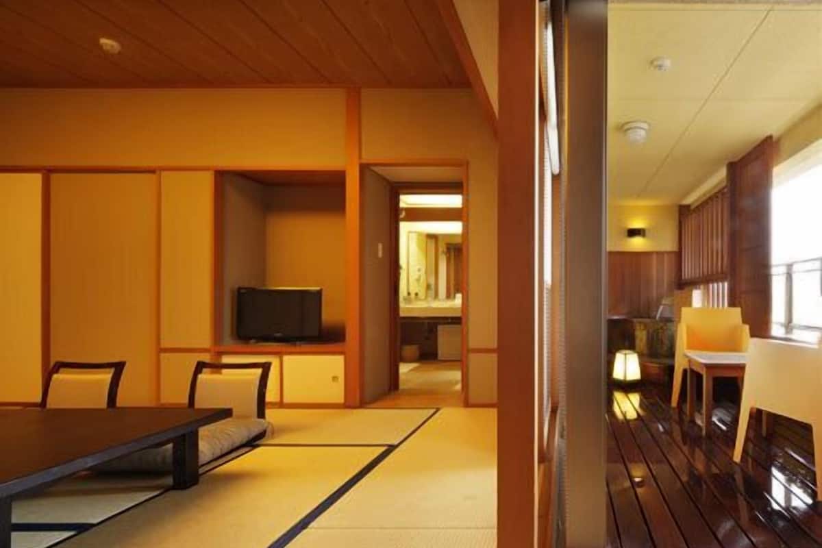 A traditional Japanese-style room with tatami flooring, a low table, chairs, and a television.