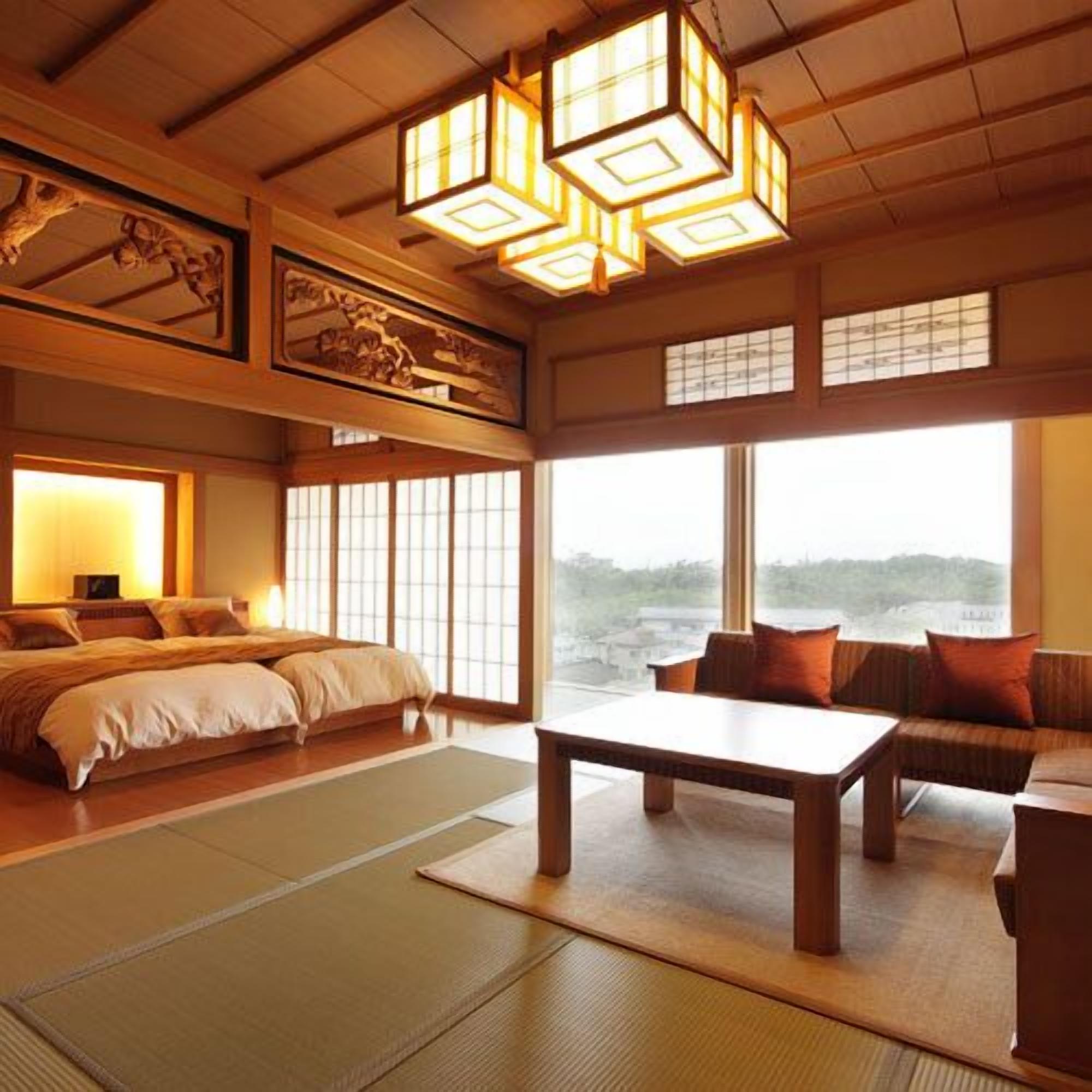 A traditional Japanese-style room with tatami flooring, a low wooden bed, a sofa, a table, and a view of the sea.