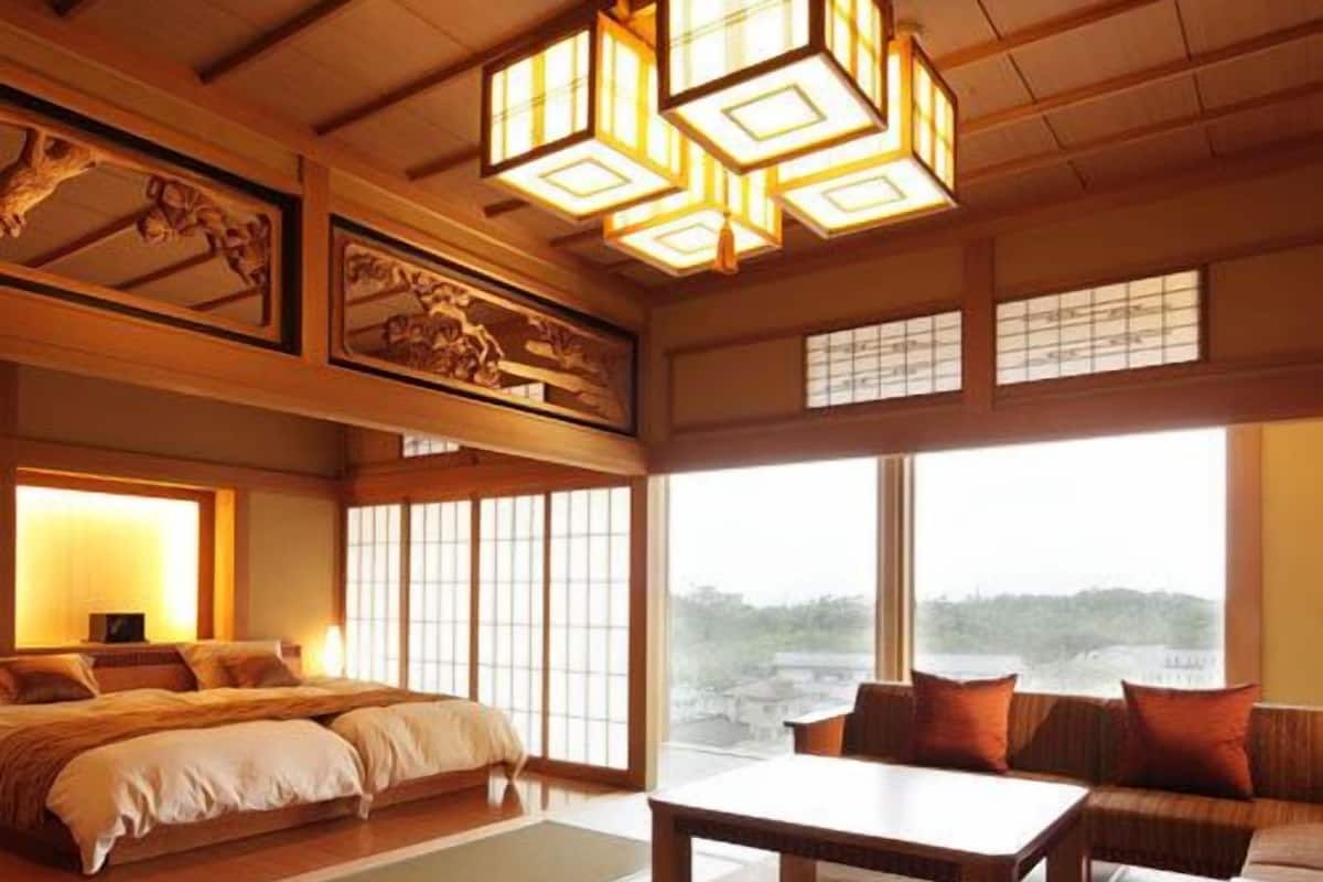 A traditional Japanese-style room with tatami flooring, a low wooden bed, a sofa, a table, and a view of the sea.