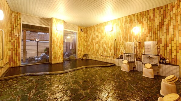 Un onsen japonais traditionnel, avec un sol en pierre, des murs en bois et un miroir qui reflète l’intérieur.