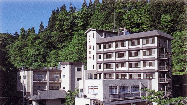 Un edificio de varios pisos con techo plano, rodeado de un bosque denso.
