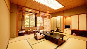 Une pièce de style japonais traditionnel, avec un sol recouvert de tatamis, une table basse, des chaises, un téléviseur et des portes coulissantes.