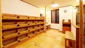 A room with wooden shelves filled with baskets, a wooden bench, a clock on the wall, and a small table with a lamp.