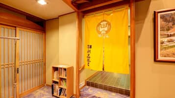 A traditional Japanese room with tatami flooring, a bookshelf, a futon bed, and a sliding door with a yellow curtain.