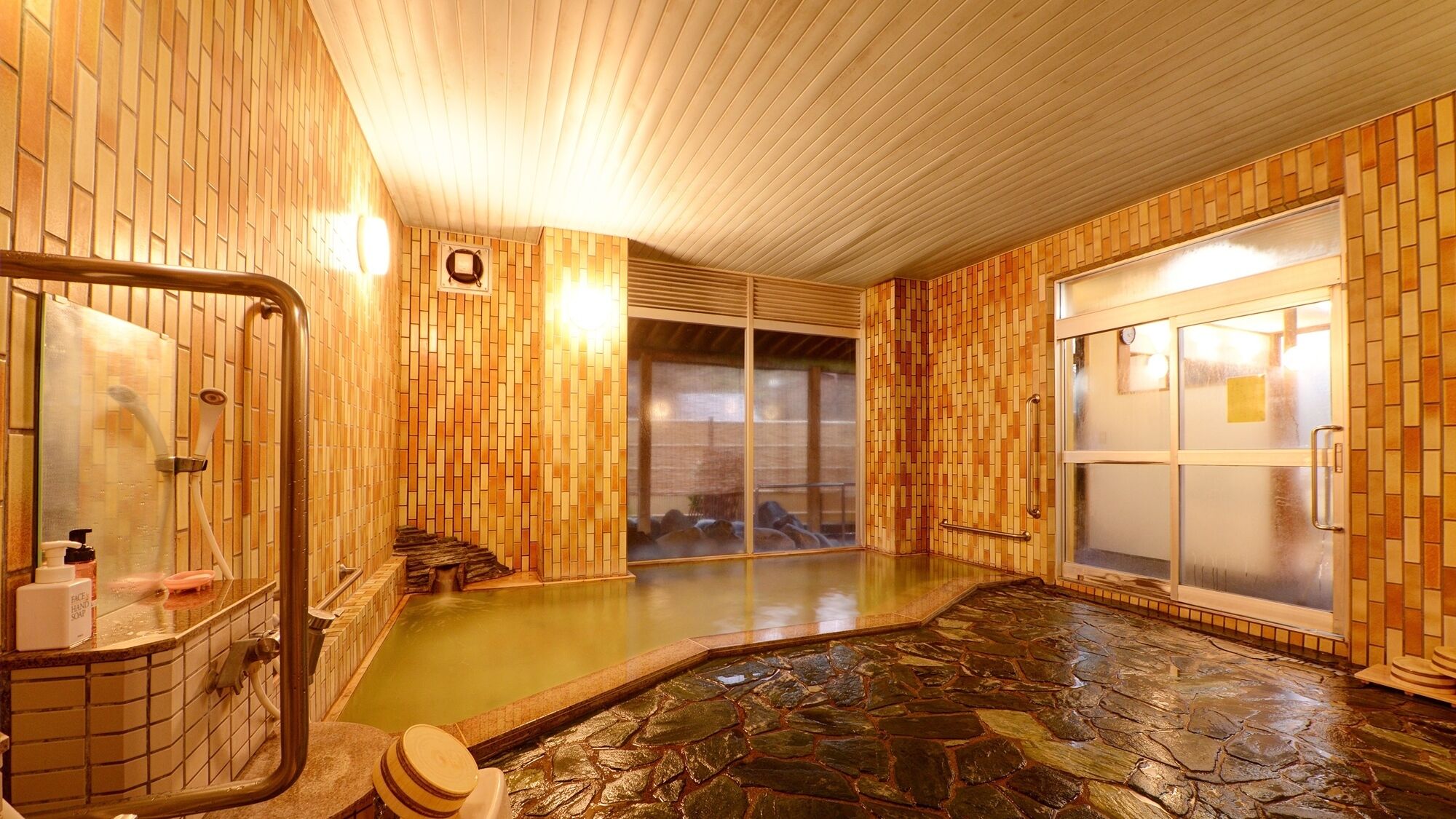 A traditional Japanese onsen with wooden walls, a stone bath, and a sliding glass door.