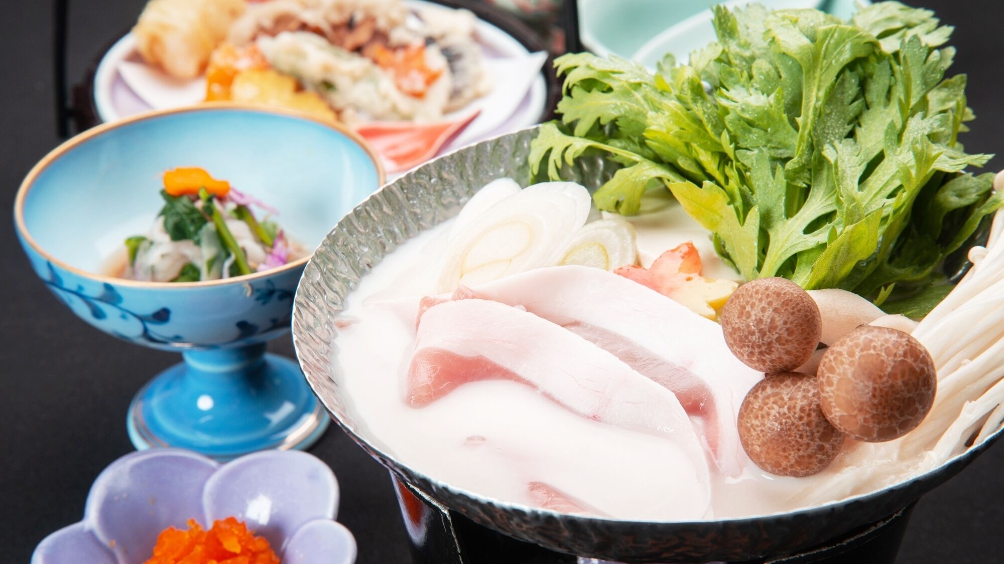 A bowl of food with various ingredients, a blue bowl with a floral pattern, and a plate with food in the background.