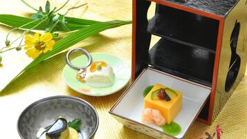 Preparación tradicional de ceremonia del té japonesa con un cuenco, un plato pequeño con polvo verde, un pastel de arroz mochi y una caja con una hoja verde.