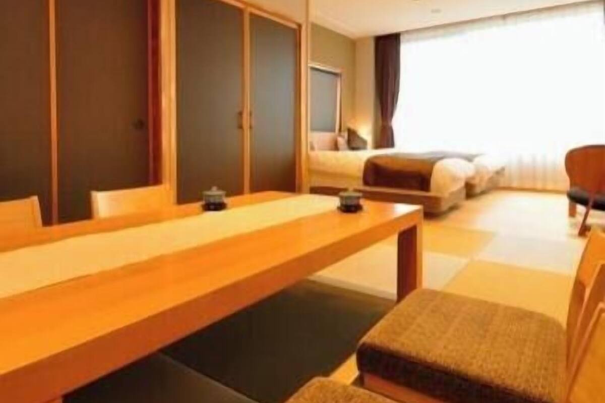 A hotel room with a wooden desk, a sofa, a bed, and a large window.