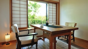 A traditional Japanese room with tatami flooring, a wooden table, two chairs, a sliding shoji screen, and a small table lamp.