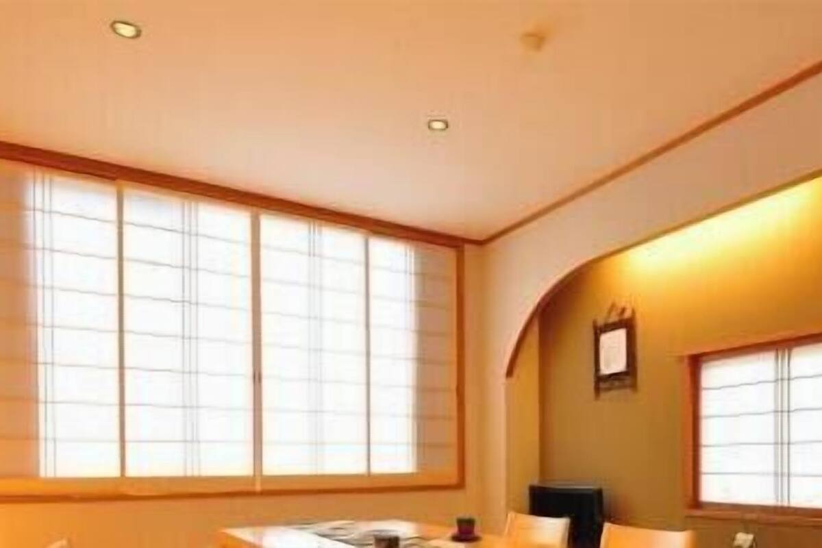 A hotel room with large windows, a desk, and a chair.