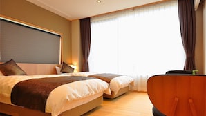 A hotel room with two beds, a wooden floor, a desk, and a chair.