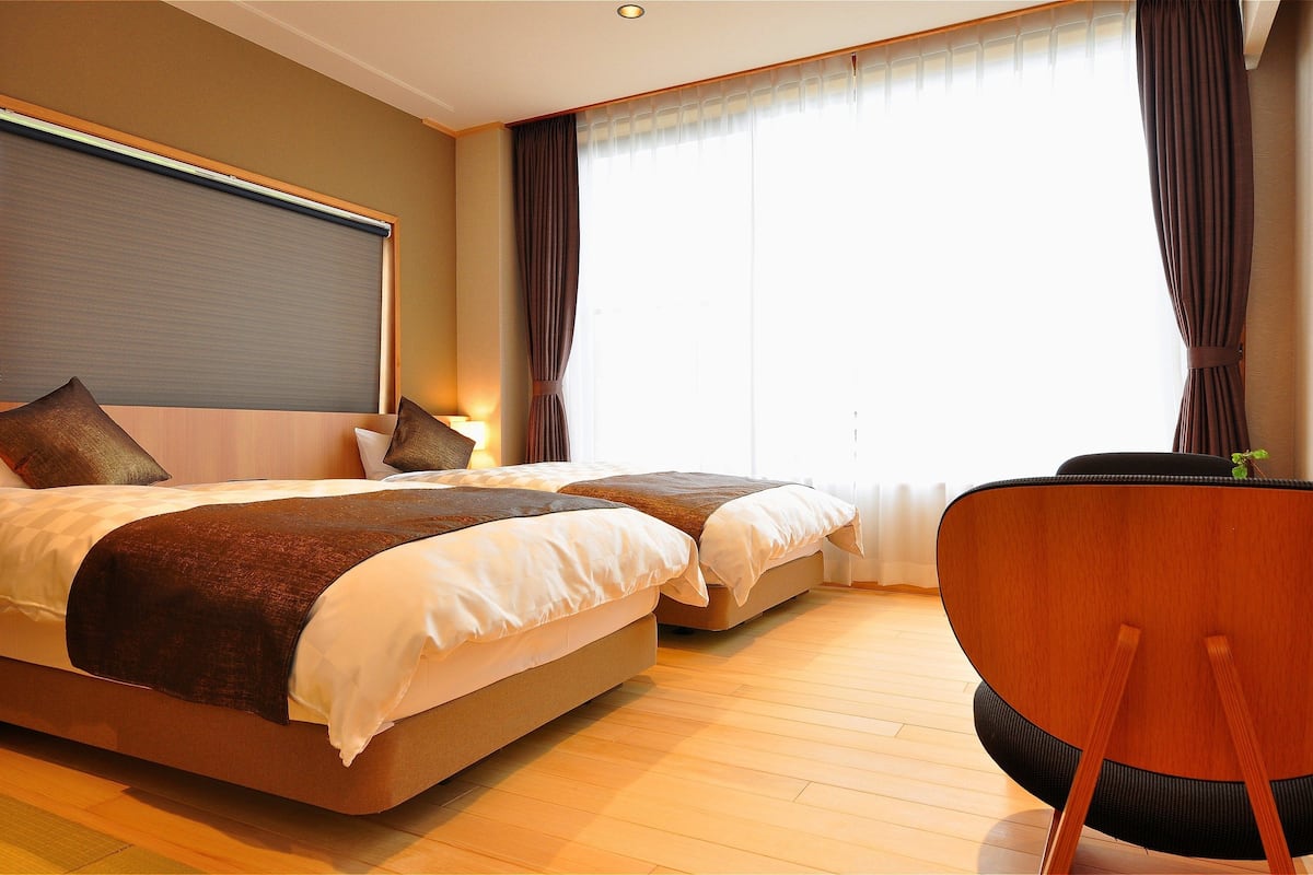 A hotel room with two beds, a wooden floor, a desk, and a chair.