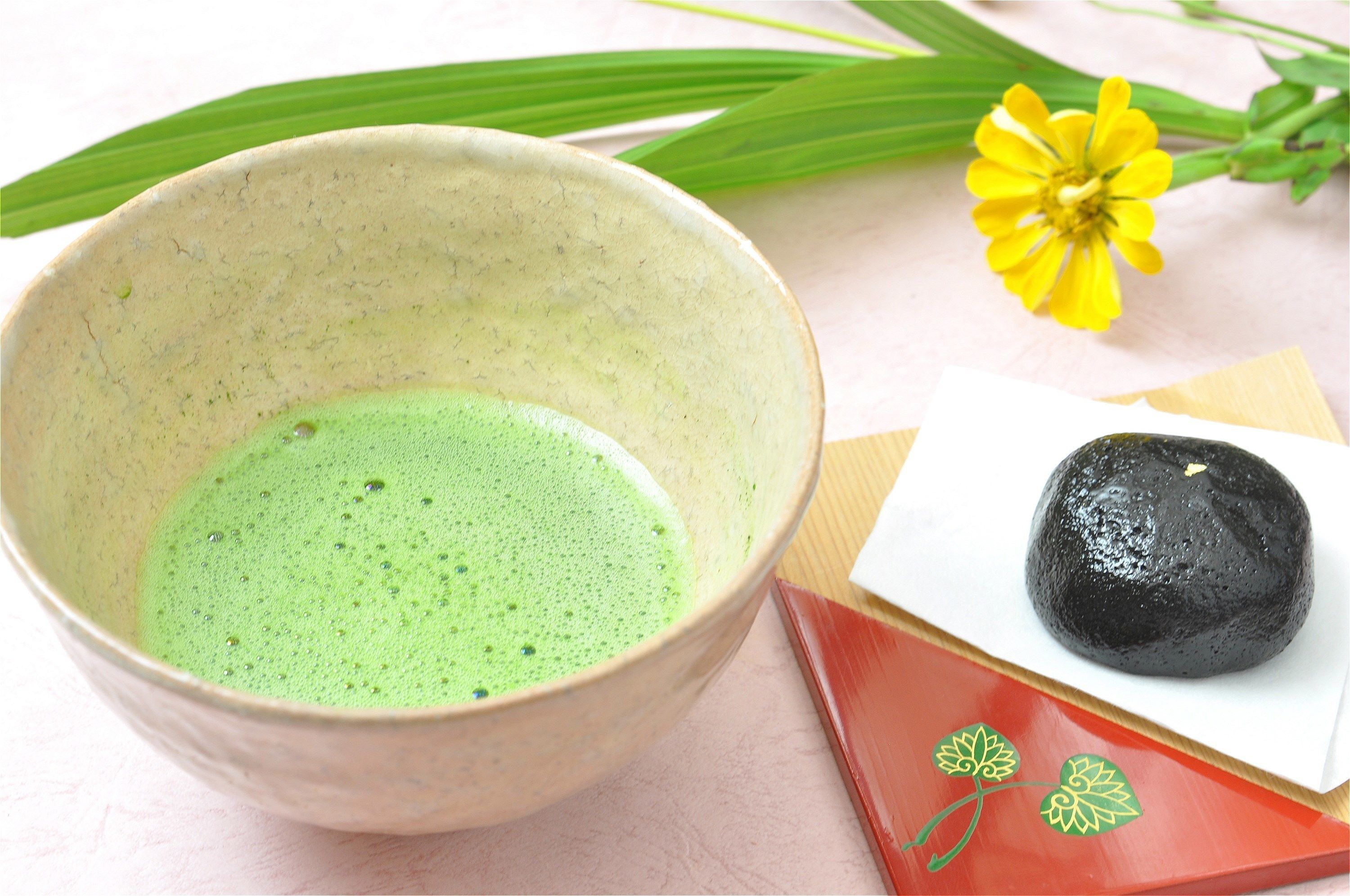 A bowl of green liquid, a black round object, and a yellow flower.