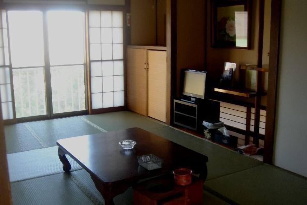 Une pièce de style japonais traditionnel, avec un sol recouvert de tatamis, une table basse, un téléviseur et une porte coulissante.