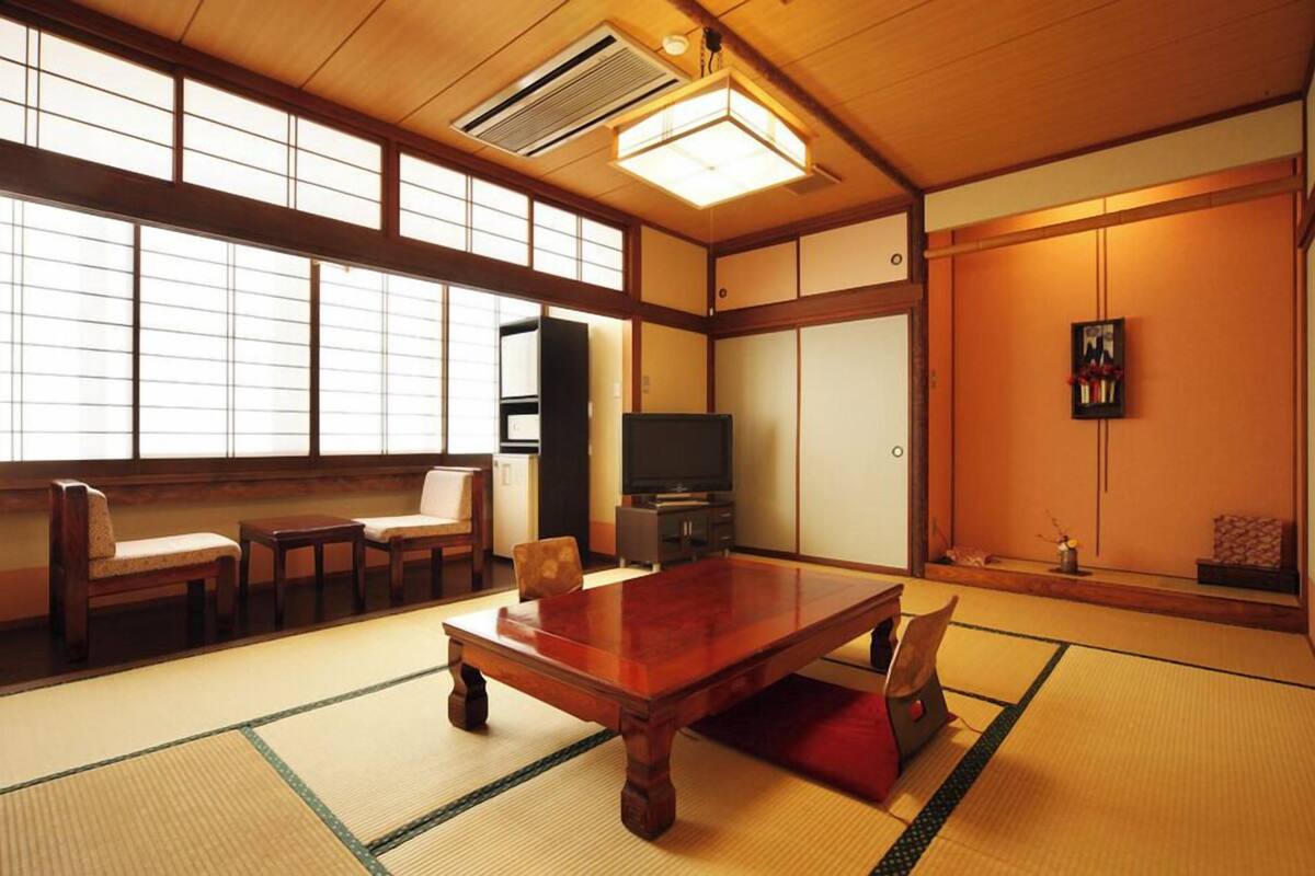 Une pièce de style japonais traditionnel, avec un sol recouvert de tatamis, une table basse, des chaises, un téléviseur et des portes coulissantes.