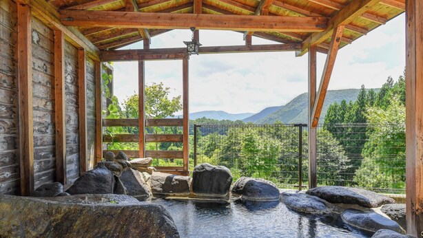 A wooden cabin with a hot spring area, surrounded by rocks and a metal fence, overlooking a mountainous landscape. - Shiobara Onsen Yuyado Umekawaso (Nasushiobara)