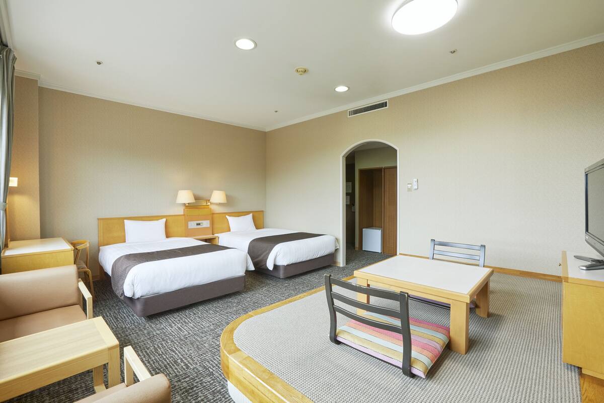 Une chambre d’hôtel avec deux lits, un bureau, une chaise, une télévision et une petite table.