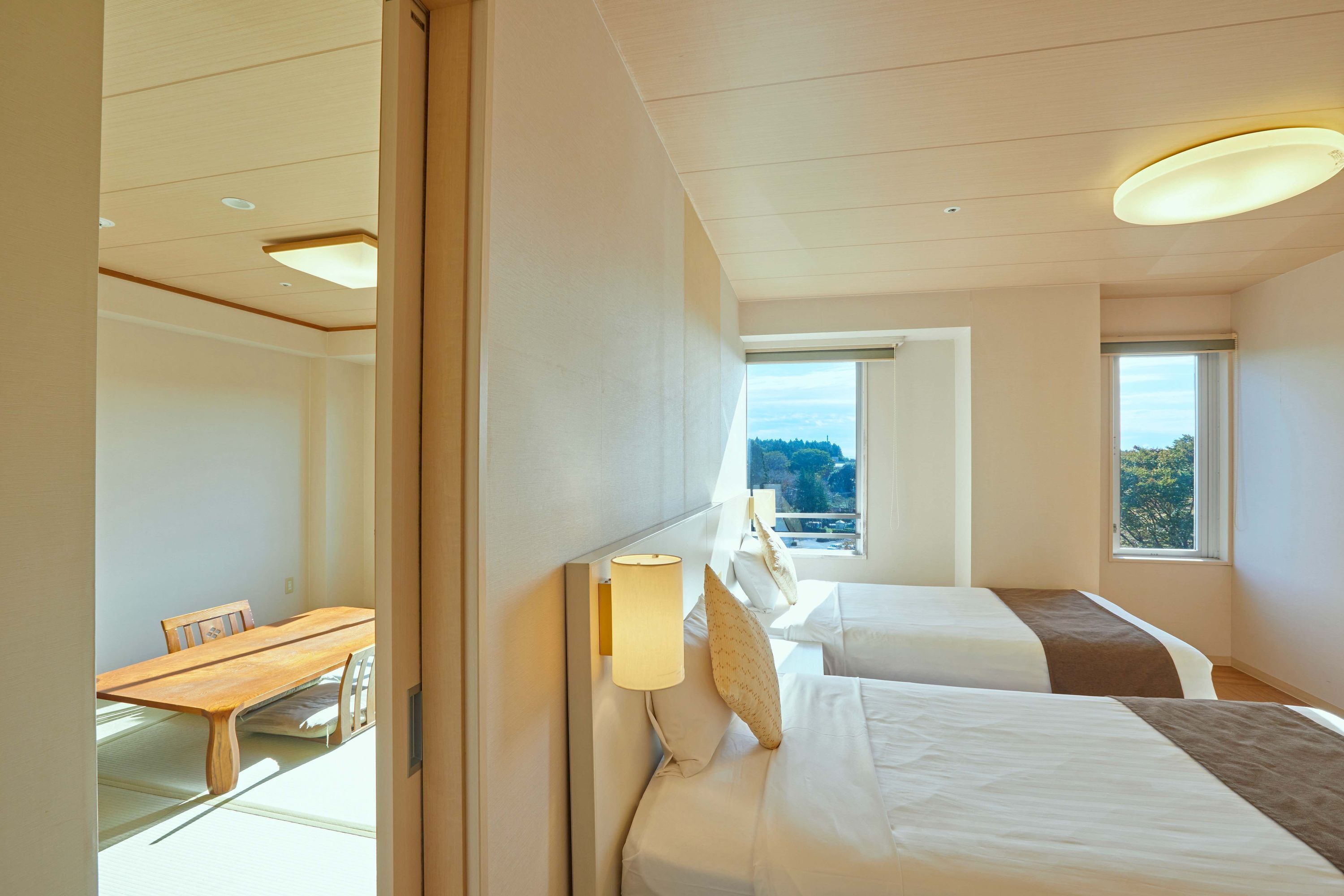 A hotel room with two beds, a dining table, and a view of the outdoors.