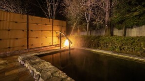 Une piscine en pierre, entourée d’une clôture en bois, avec des arbres en arrière-plan.