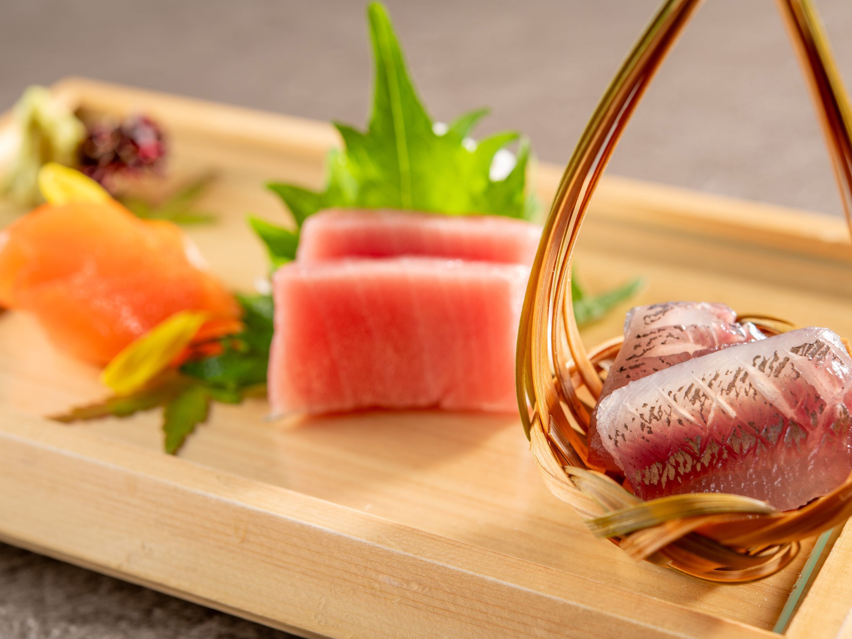A wooden serving tray with various sashimi pieces and a woven basket.