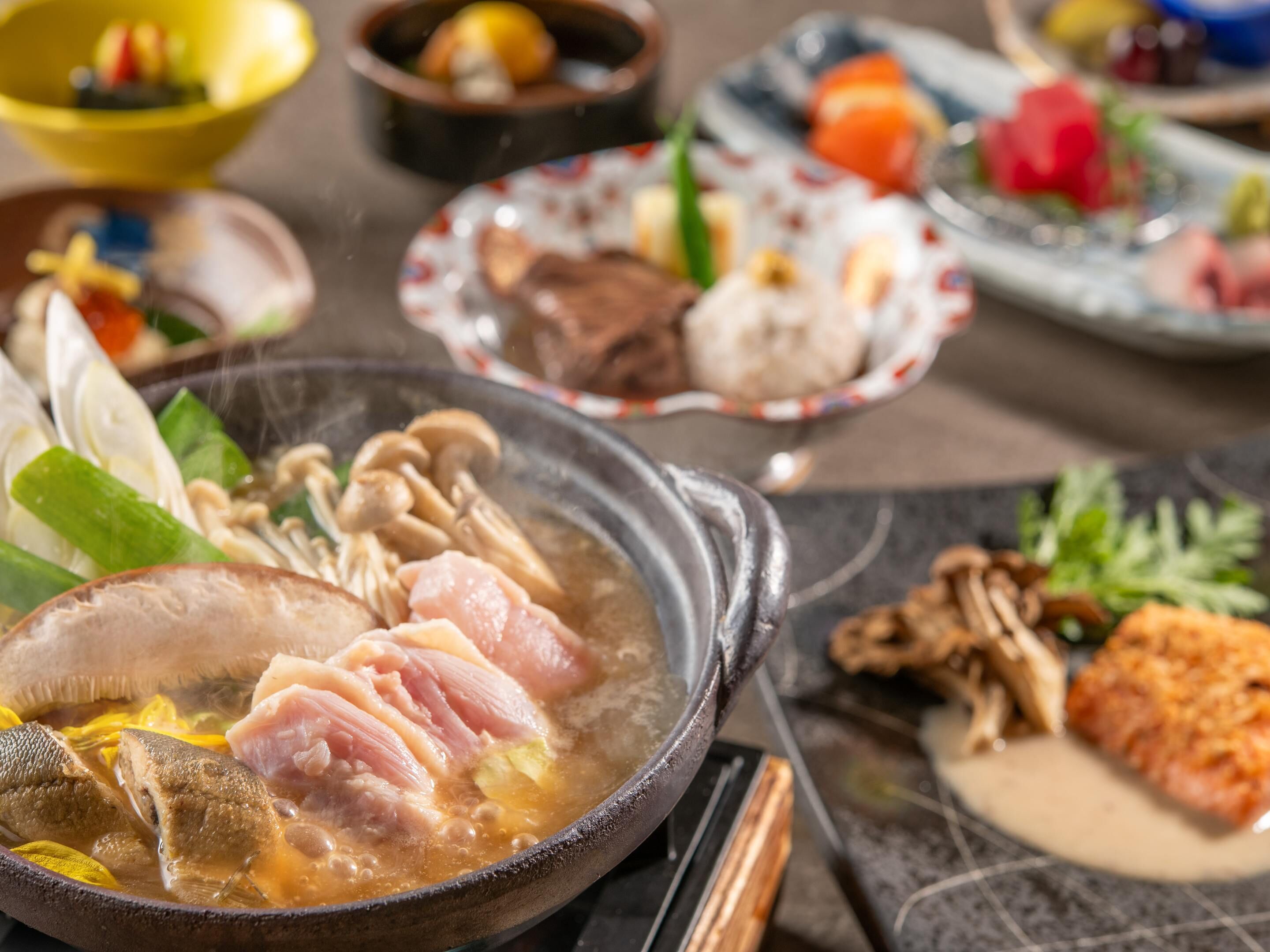 Una mesa de comedor con varios platos, incluyendo un tazón de sopa con carne y verduras, un plato con un trozo de pescado y otros alimentos.
