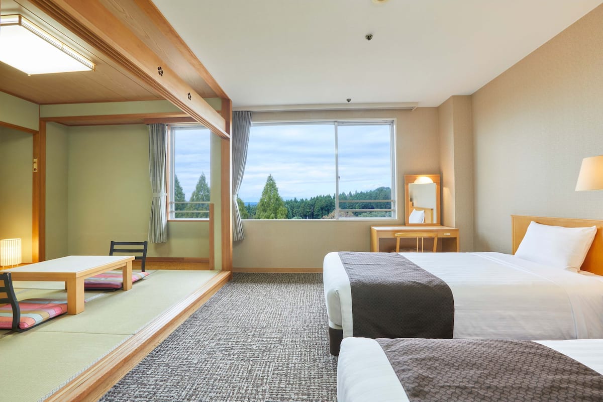 Une chambre d’hôtel comprenant un lit, un bureau, une chaise, une fenêtre donnant sur des arbres et un sol recouvert de moquette.