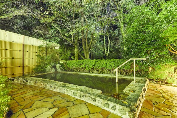 Un espace extérieur pavé de pierres, avec une petite piscine, entouré d’une végétation luxuriante et d’une clôture en bambou.