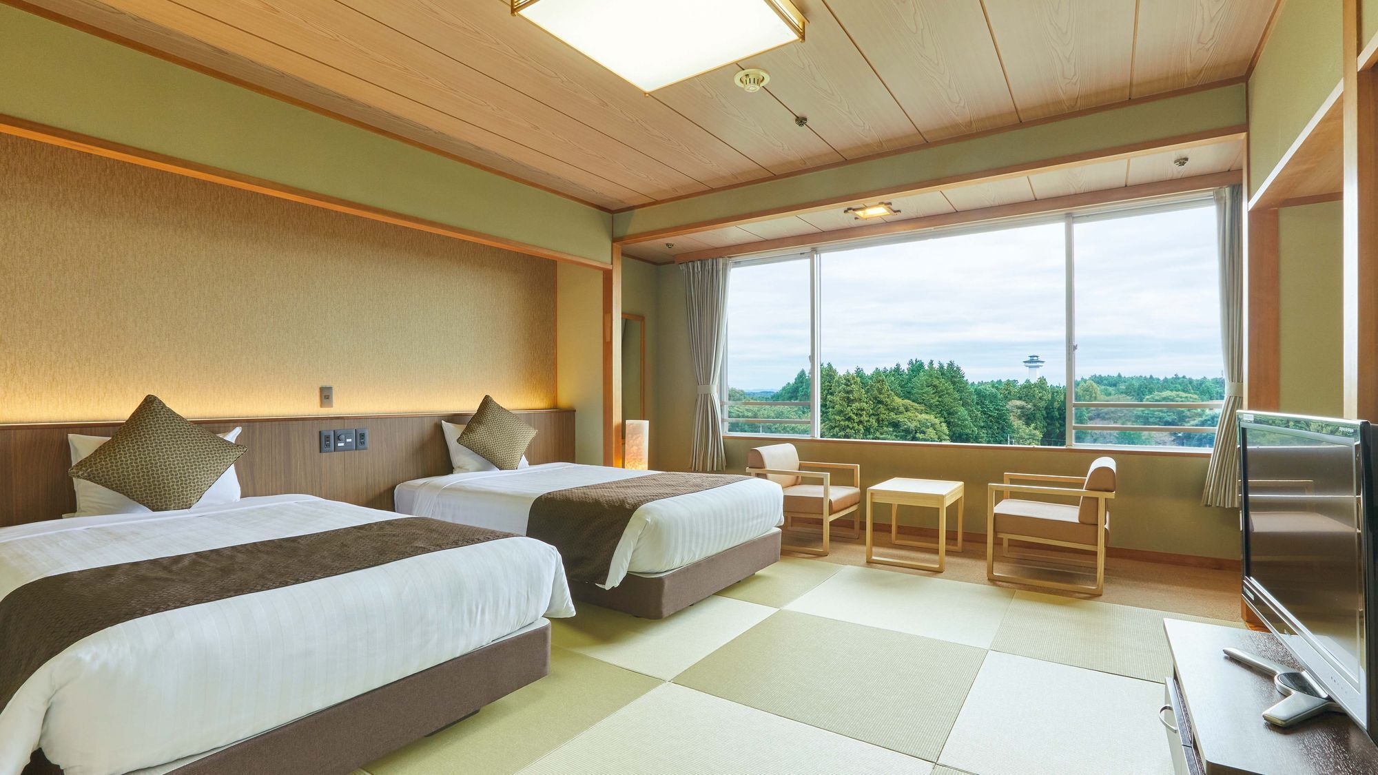 Ein Hotelzimmer mit zwei Betten, einem kleinen Tisch, Stühlen, einem Fernseher und einem großen Fenster mit Blick.