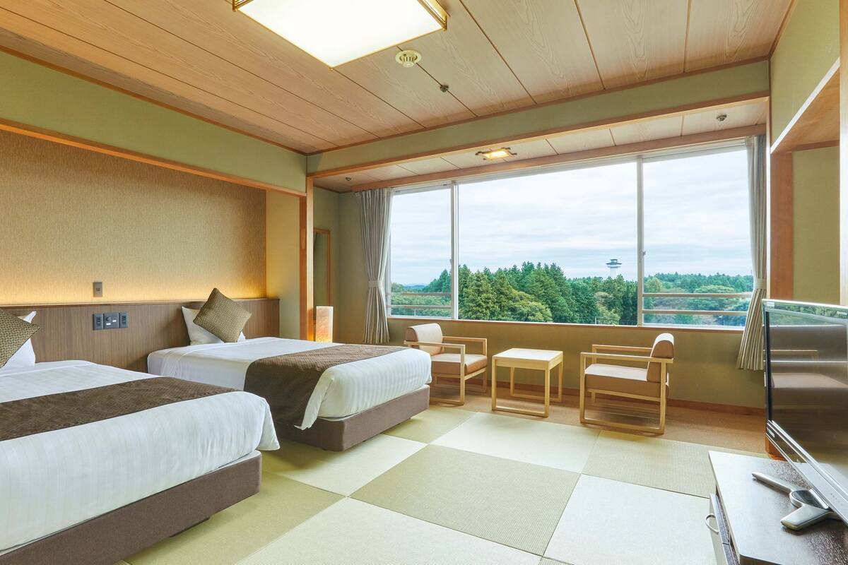 Une chambre d’hôtel avec deux lits, une petite table, des chaises, une télévision et une grande fenêtre donnant sur un beau paysage.