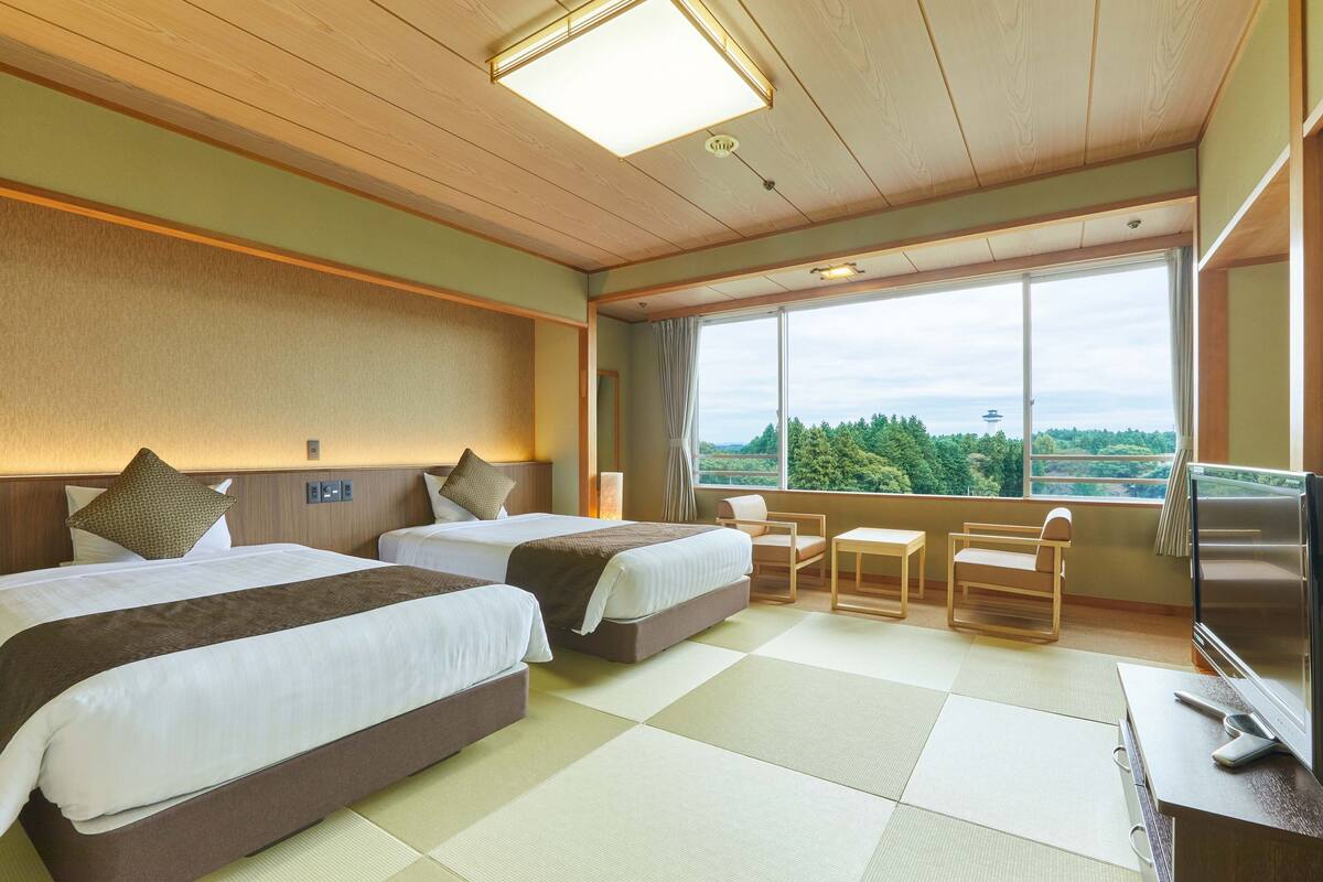 Une chambre d’hôtel avec deux lits, une télévision, un bureau et une grande fenêtre donnant sur l’extérieur.