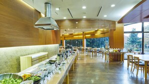 Un espace buffet doté de plusieurs présentoirs de nourriture, d’un plancher en bois et de grandes fenêtres offrant une vue sur les arbres.