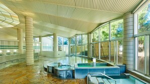 Un vaste espace intérieur abritant une piscine, doté d’un sol en pierre, de grandes fenêtres et d’un plafond haut orné d’un motif en réseau.