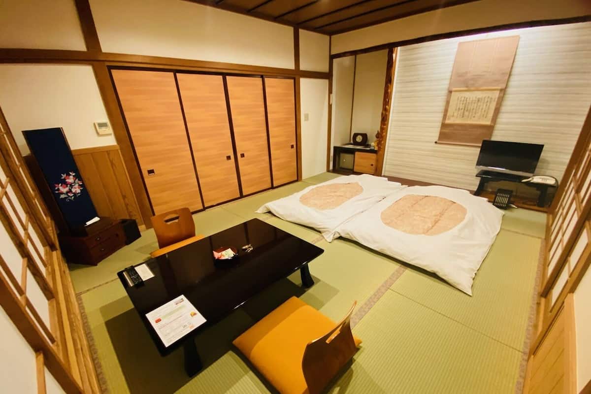 A traditional Japanese room with tatami flooring, a futon bed, a low table with a menu, a wooden cabinet, and a television.